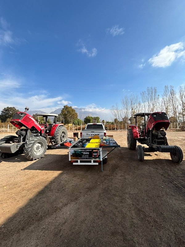Dos tractores rojos y el tráiler de servicio en un campo