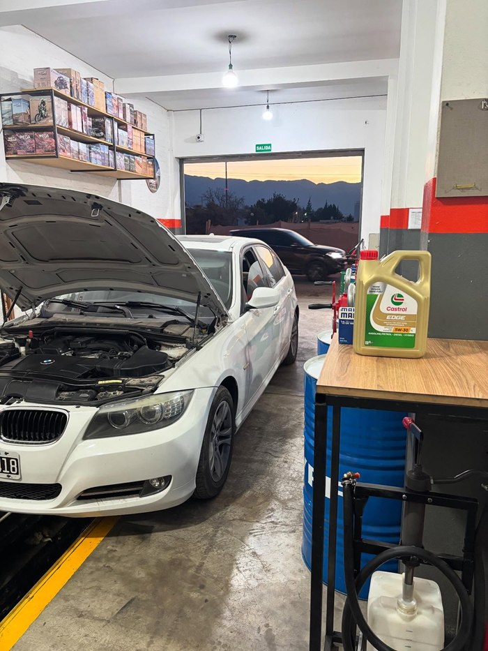 BMW blanco con el capó abierto junto a un bidón de aceite Castrol