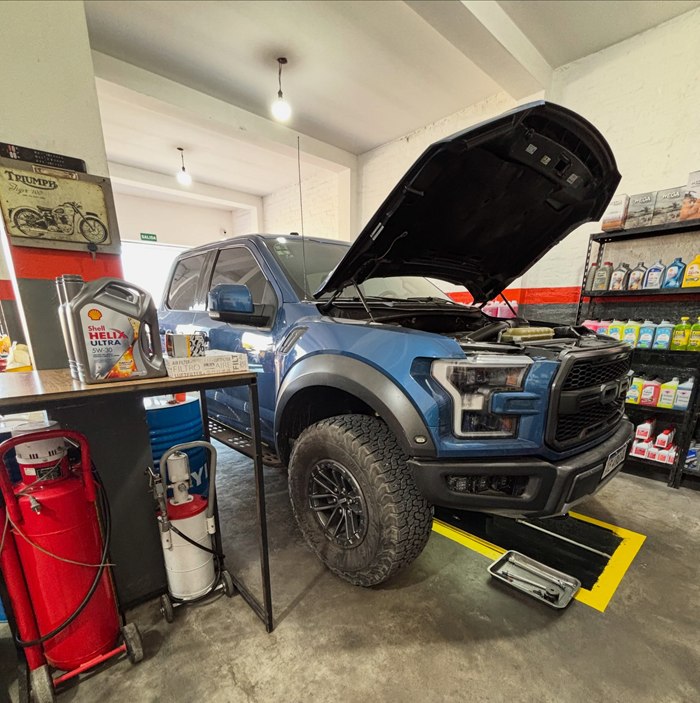 Ford F-150 Raptor azul con el capó abierto junto a bidones de Shell Helix Ultra